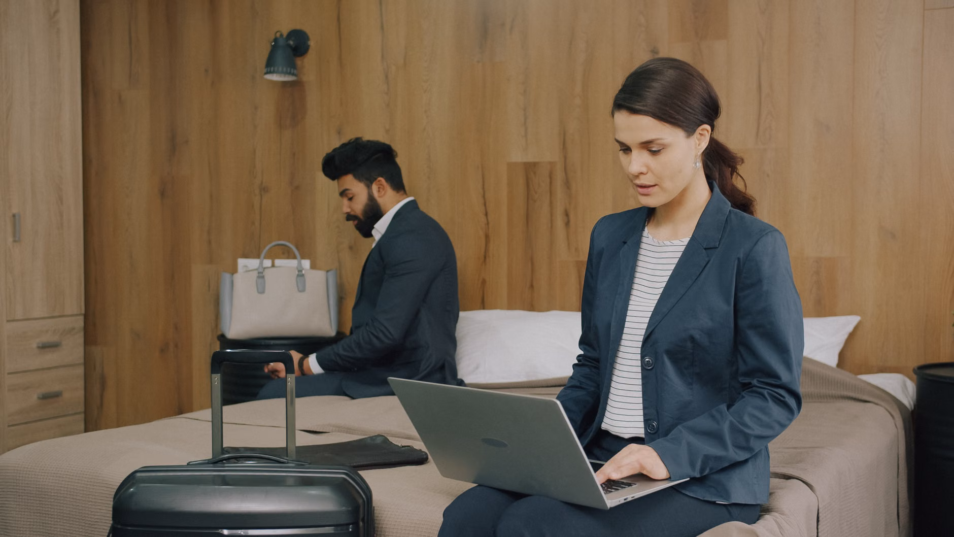 Due professionisti lavorano al computer portatile in una camera d'albergo, a dimostrazione del moderno stile di vita da viaggiatore.