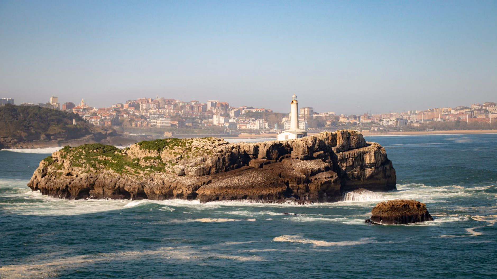 Malerscher Blick auf die Insel Mouro und ihren Leuchtturm mit der Skyline von Santander im Hintergrund, Spanien.