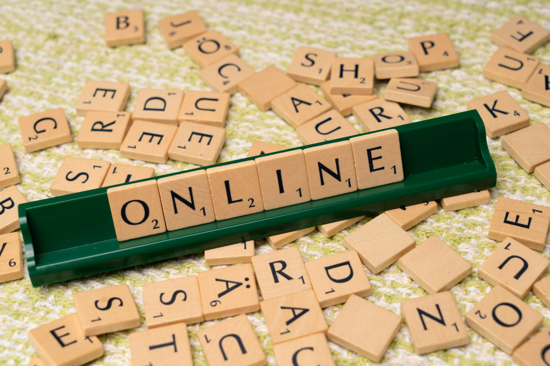 Scrabble-Steine, die 'online' auf einem grünen Tablett buchstabieren, um digitale Konnektivität und Sprache zu symbolisieren.