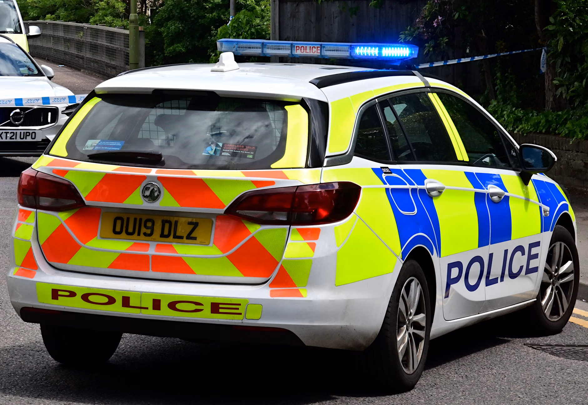 Rückansicht eines britischen Polizeiautos mit blinkenden blauen Lichtern auf einer Stadtstraße, die die Rechtsdurchsetzung gewährleistet.