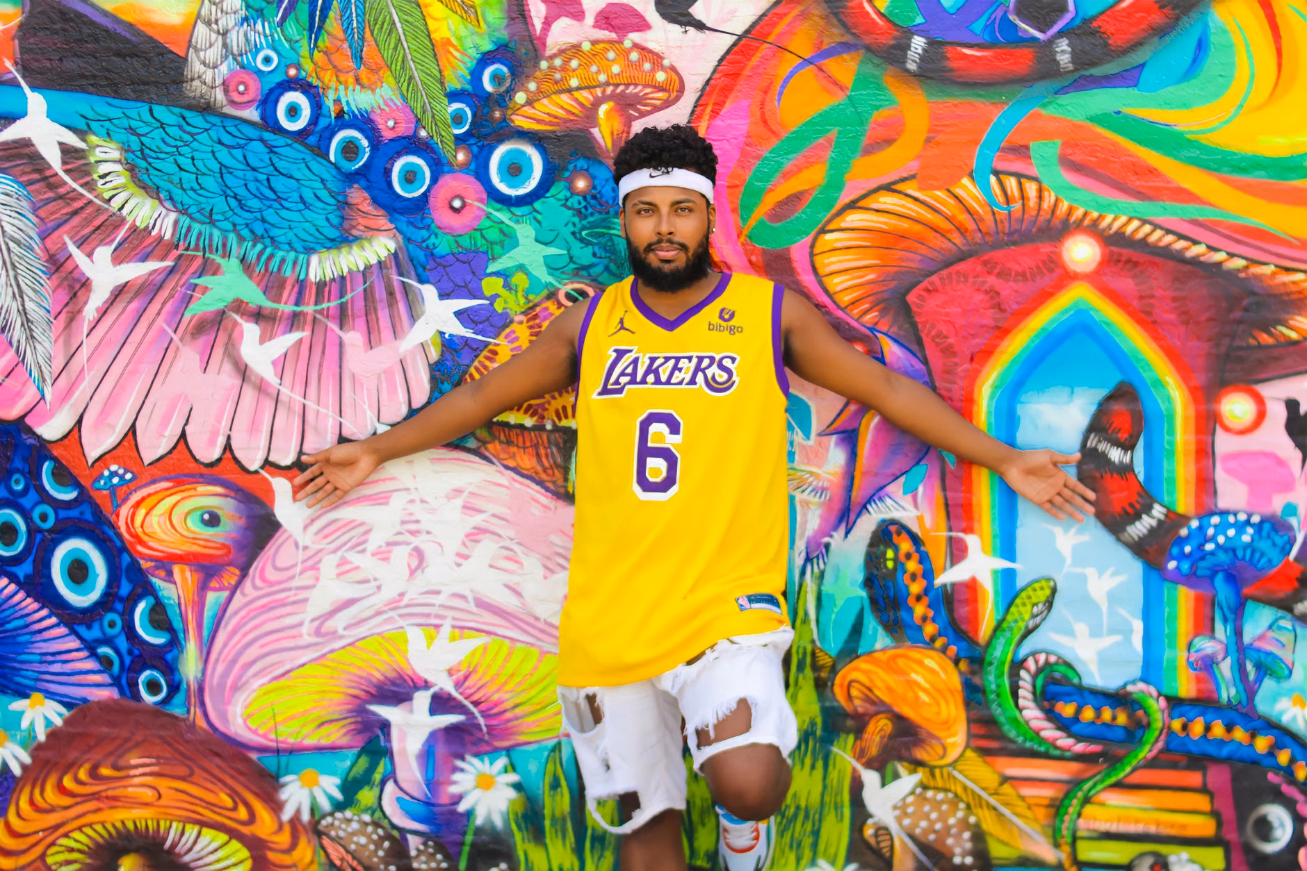 Man in Lakers jersey posing against a colorful mural wall, showcasing vibrant art and style.