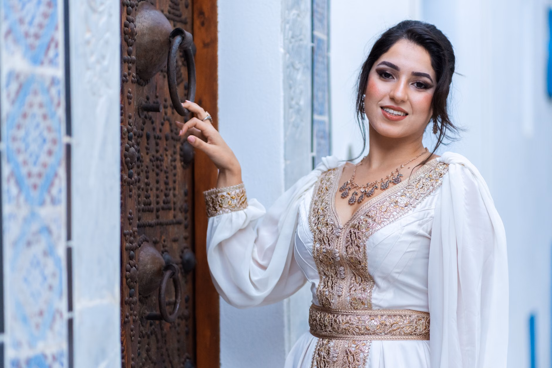 Portrait d'une femme en tenue traditionnelle posant à côté d'une porte ornée avec des motifs complexes.