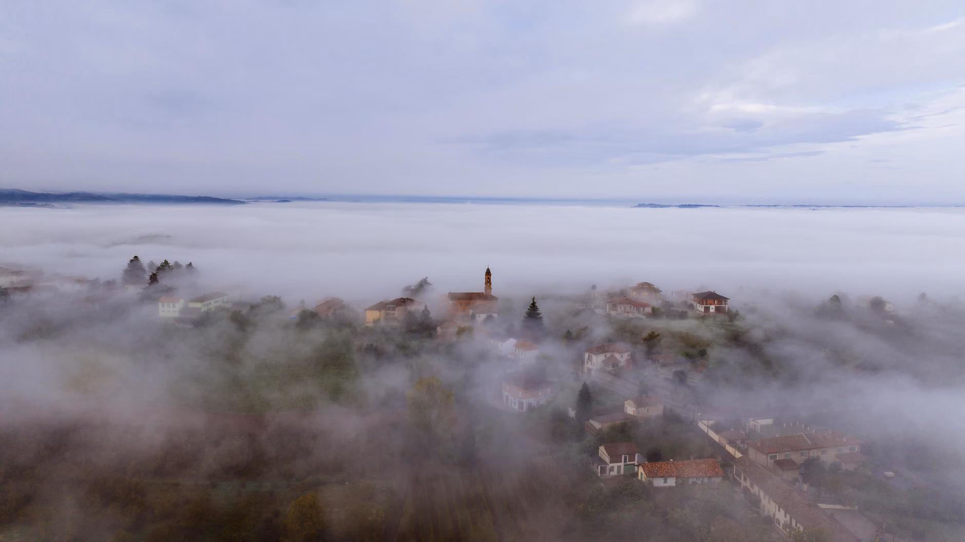 A serene aerial view of Annunziata village shrouded in fog, showcasing Italian countryside charm.
