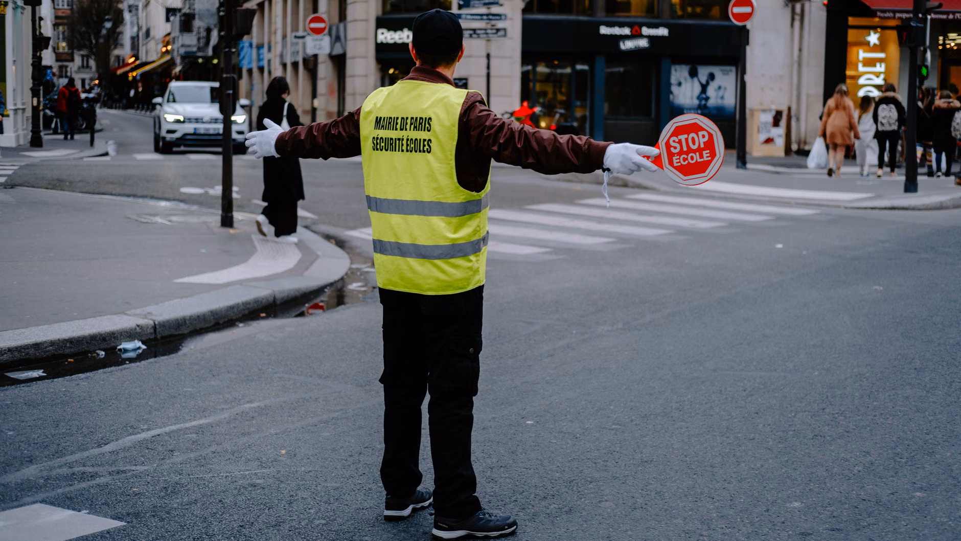 Vue de dos d'un agent de passage tenant un panneau stop dans une rue animée de la ville.