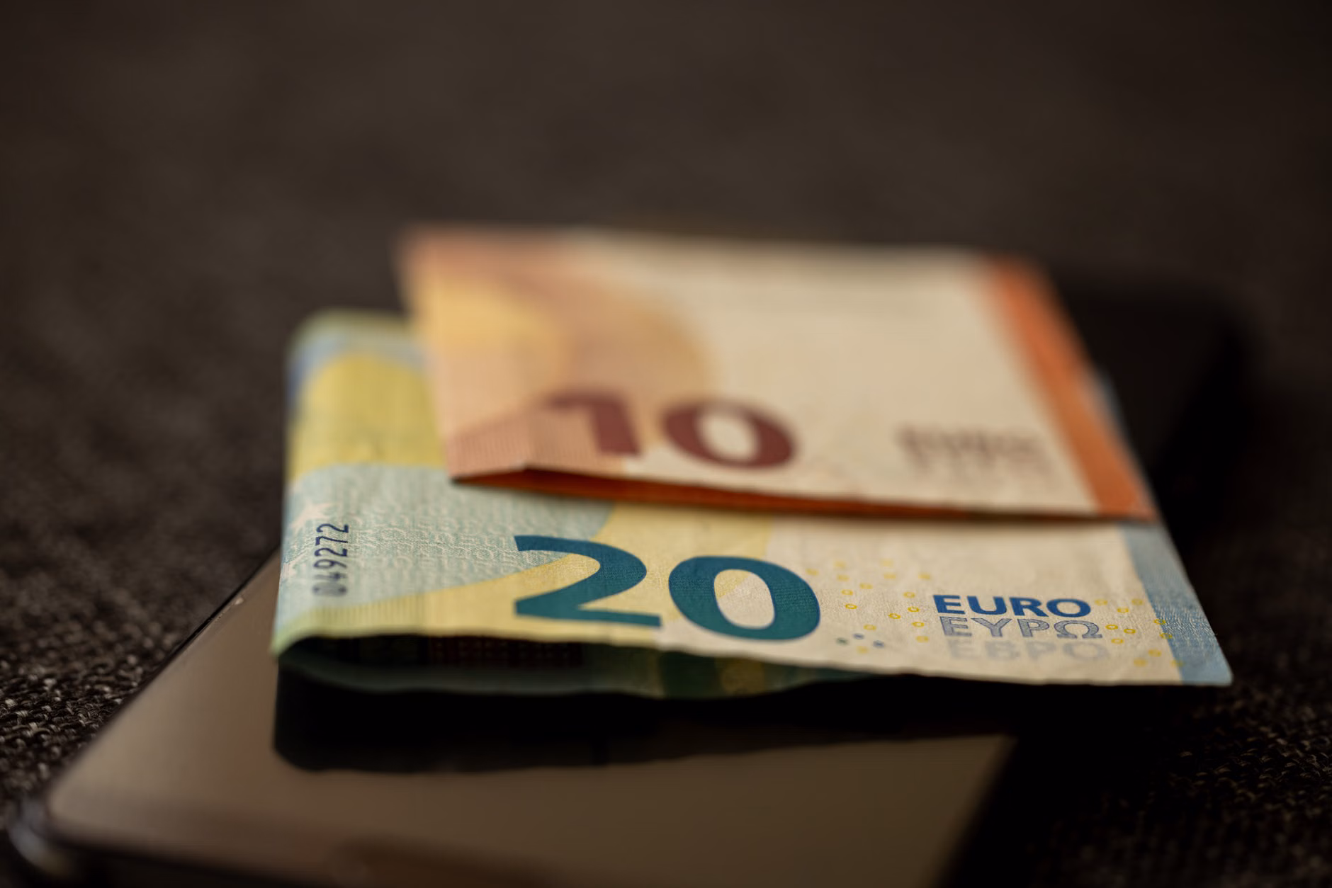 Részletes közeli felvétel 10 és 20 eurós bankjegyekről, amelyek egy okostelefonon helyezkednek el, a pénzügy és technológia reprezentálása.