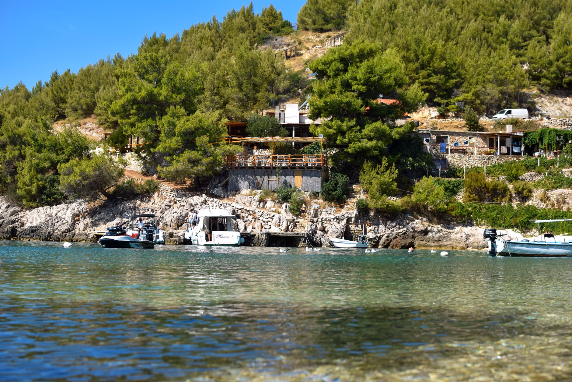 Scenic coastal landscape with boats, trees, and hillside houses on a sunny day.