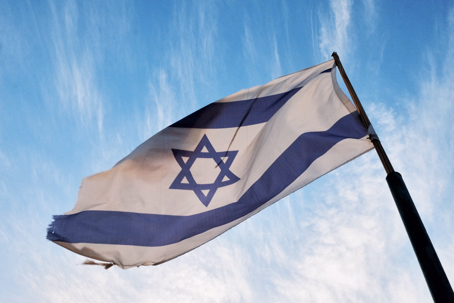 Un gros plan du drapeau israélien flottant sur un mât de drapeau contre un ciel bleu clair.