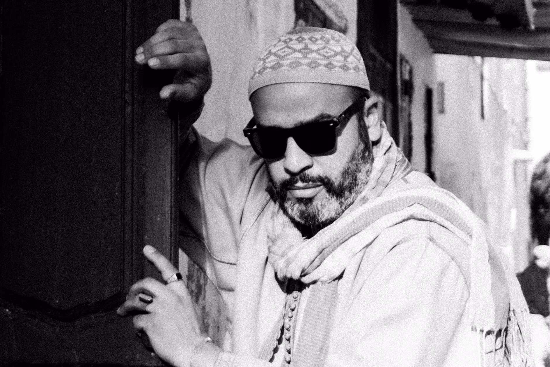 Ritratto in bianco e nero di un uomo elegante in abiti tradizionali marocchini e occhiali da sole.
