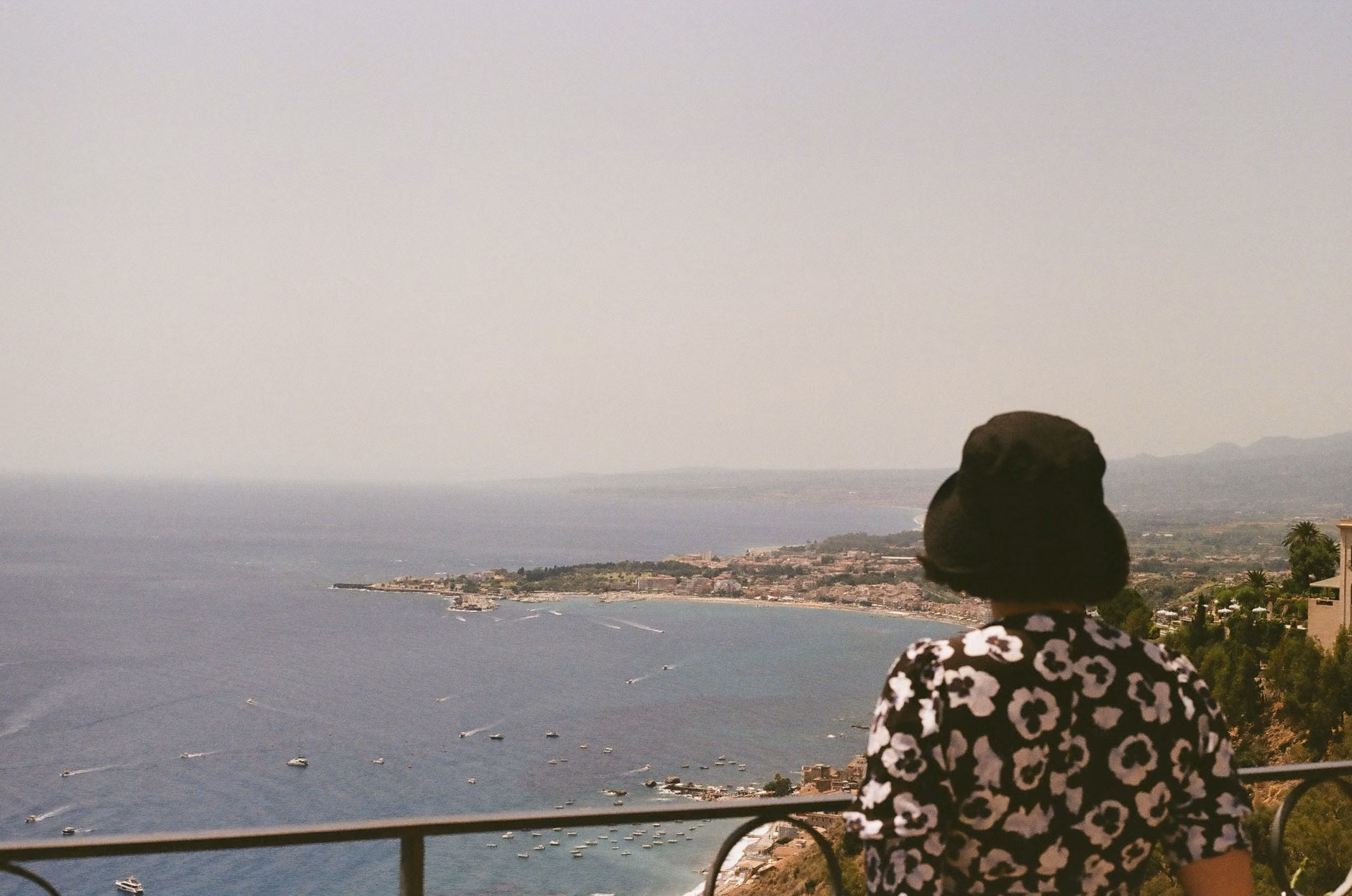 Una donna con un abito floreale ammira lo splendido panorama costiero di Taormina, in Sicilia.